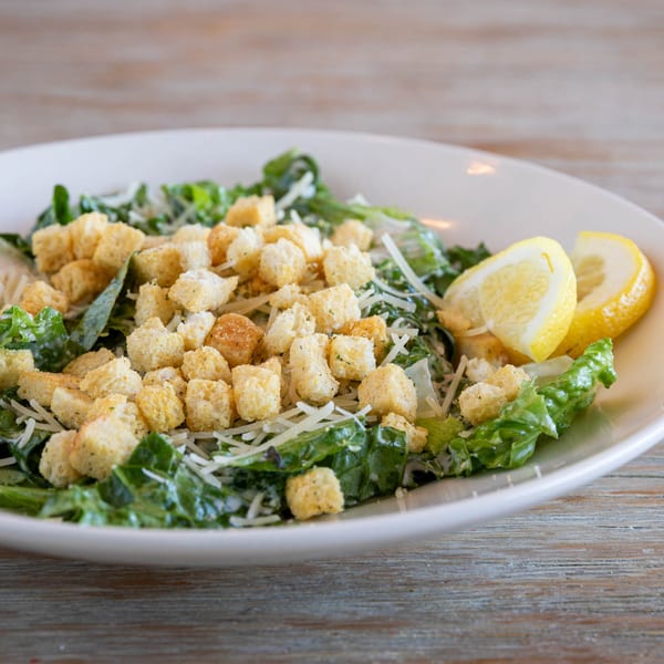 Acropolis Pizza & Pasta's Caesar salad with croutons, shredded cheese, and lemon wedges.