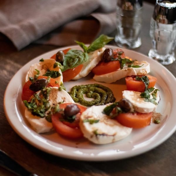 Caprese salad with mozzarella, tomatoes, basil, olives, and pesto on a white plate.