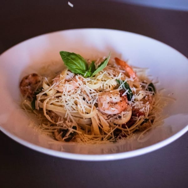 Shrimp linguine pasta with grated parmesan cheese and basil in a white bowl.