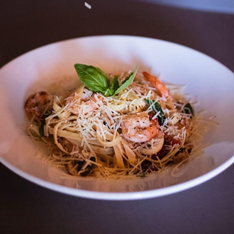 Shrimp linguine pasta with grated parmesan cheese and basil in a white bowl.