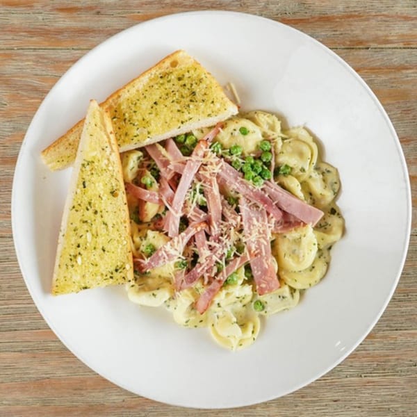 Acropolis Pizza & Pasta's tortellini with ham, peas, and garlic bread on a white plate.