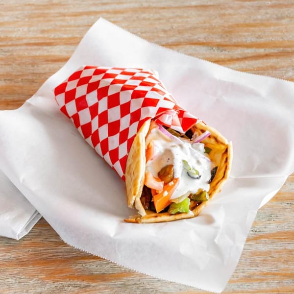 A gyro wrapped in red and white checkered paper, filled with meat, vegetables, and tzatziki sauce.