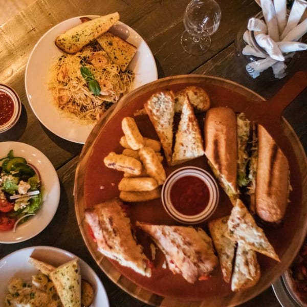 Overhead view of Italian dishes: pasta with garlic bread, salad, subs, and fried appetizers with sauce.