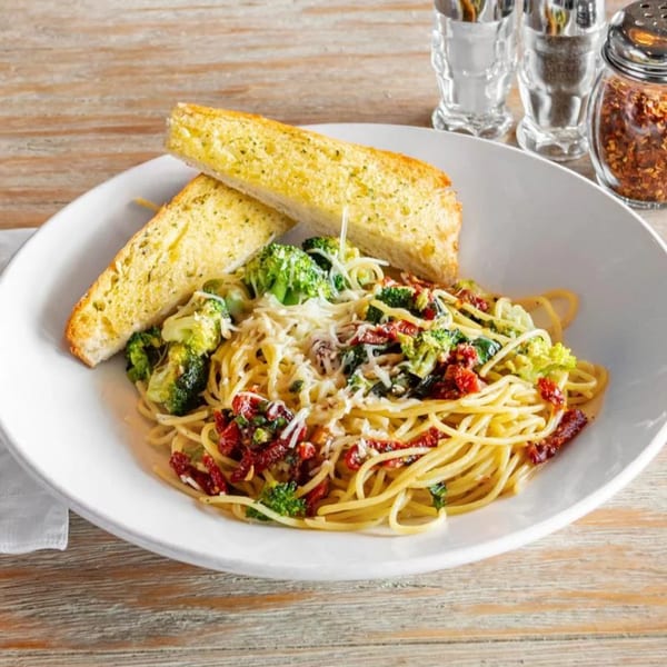 Spaghetti with broccoli, sun-dried tomatoes, and grated cheese, served with two slices of garlic bread.