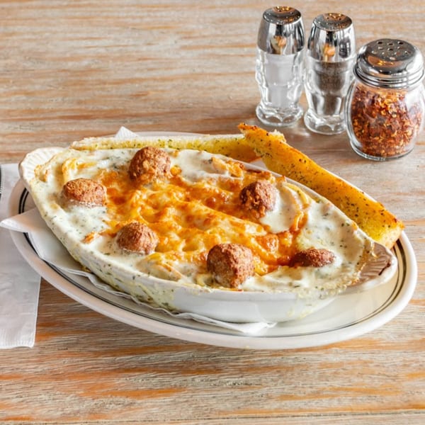 Baked pasta with meatballs and melted cheese, served with garlic bread and spices on a wooden table.